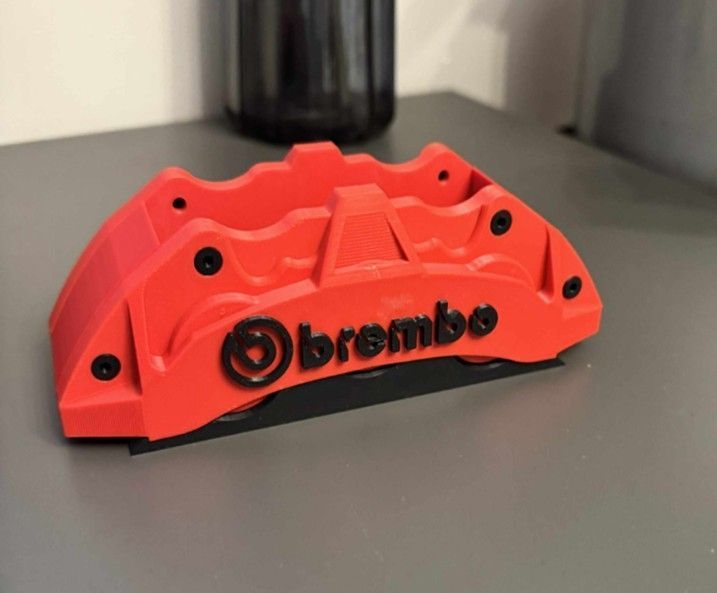 Pinza freno Brembo rosso acceso su superficie grigia, con logo e bulloni neri.