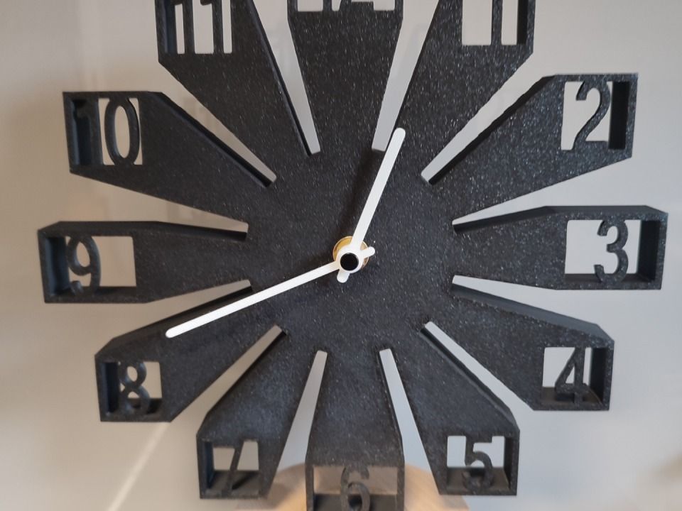 Orologio da parete decorativo nero con lancette bianche e numeri a vista su una parete chiara