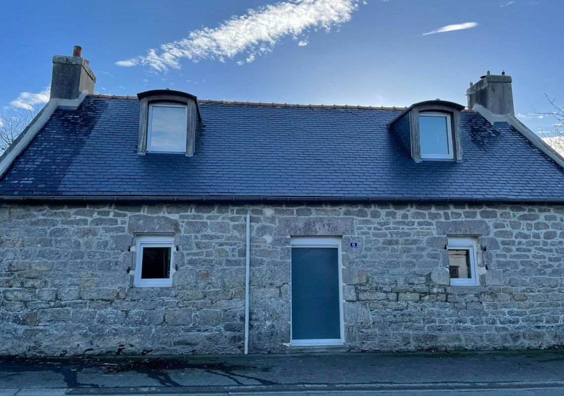Maison en pierre au toit d'ardoise, porte bleue et lucarnes.