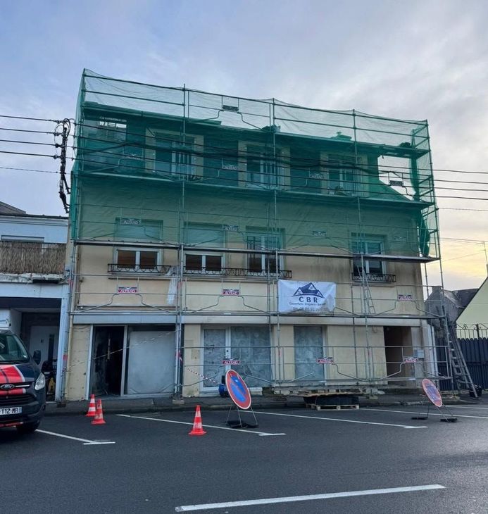 Bâtiment de trois étages en rénovation, entouré d'échafaudages avec des cônes et des filets de sécurité.