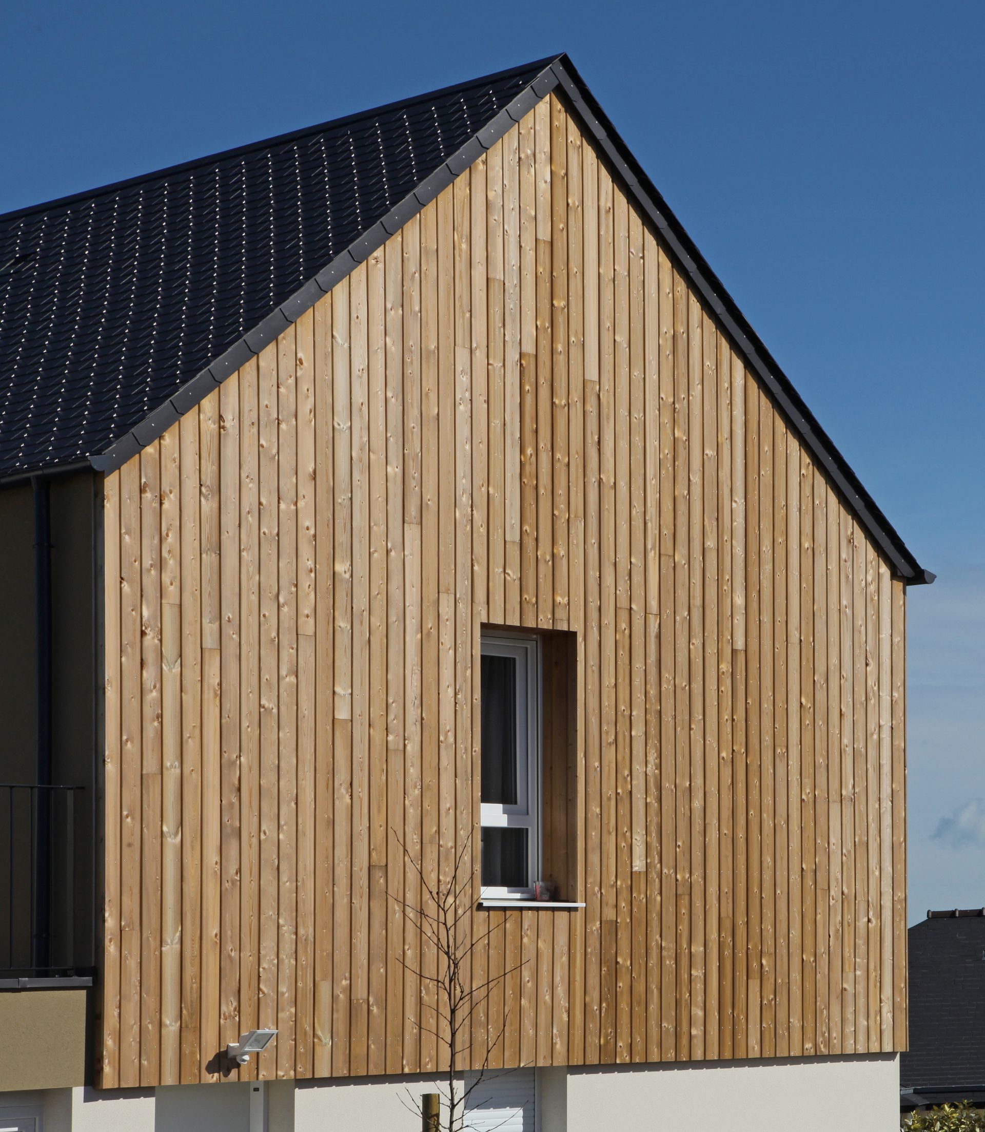 Extérieur de maison avec bardage en bois vertical, toit noir et petite fenêtre.