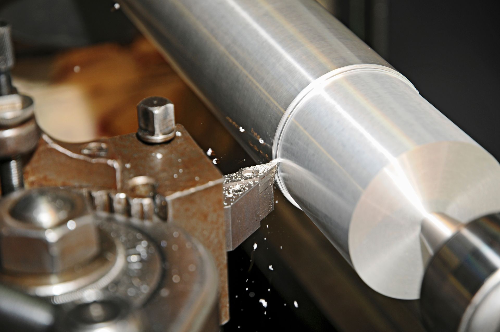Un tour à métaux usinant une pièce cylindrique brillante, avec des copeaux projetés par l’outil.
