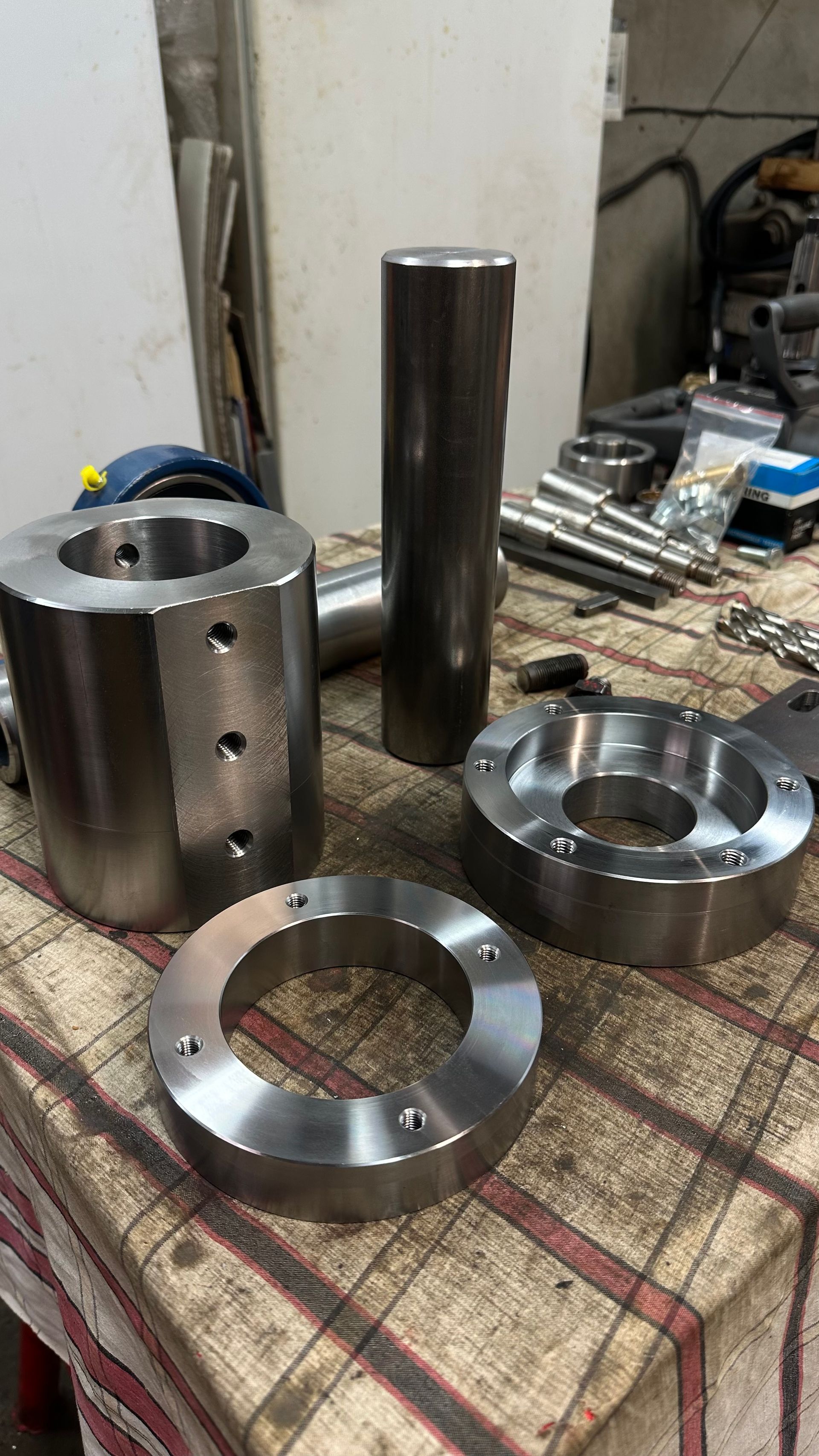 Pièces métalliques usinées posées sur une table d’atelier, notamment des composants cylindriques et annulaires.