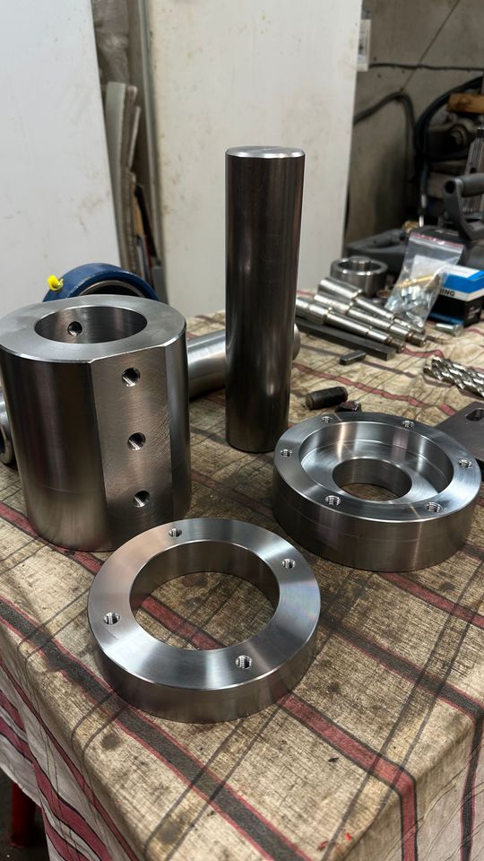 Pièces métalliques usinées posées sur une table d’atelier, notamment des composants cylindriques et annulaires.