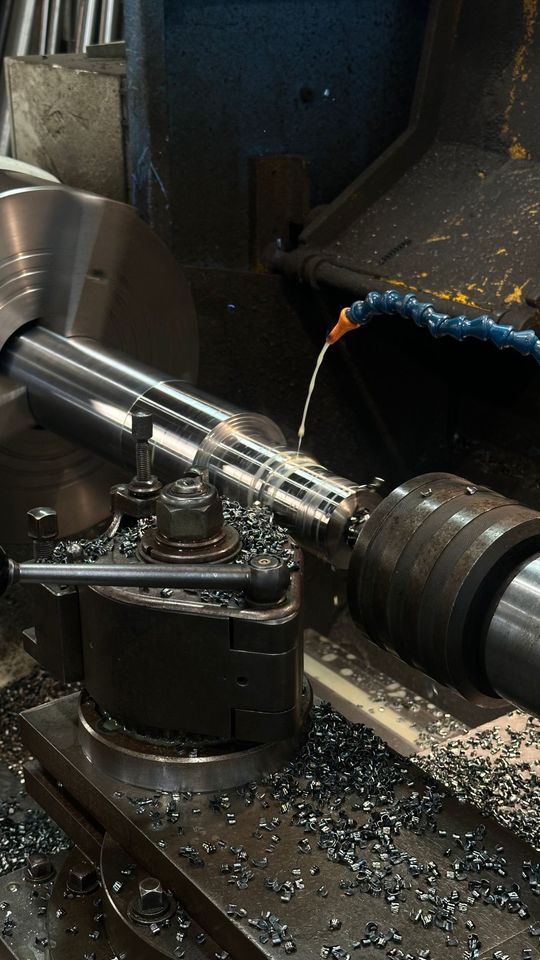 Arbre métallique usiné sur un tour, avec des copeaux et du liquide de refroidissement dans un atelier industriel.