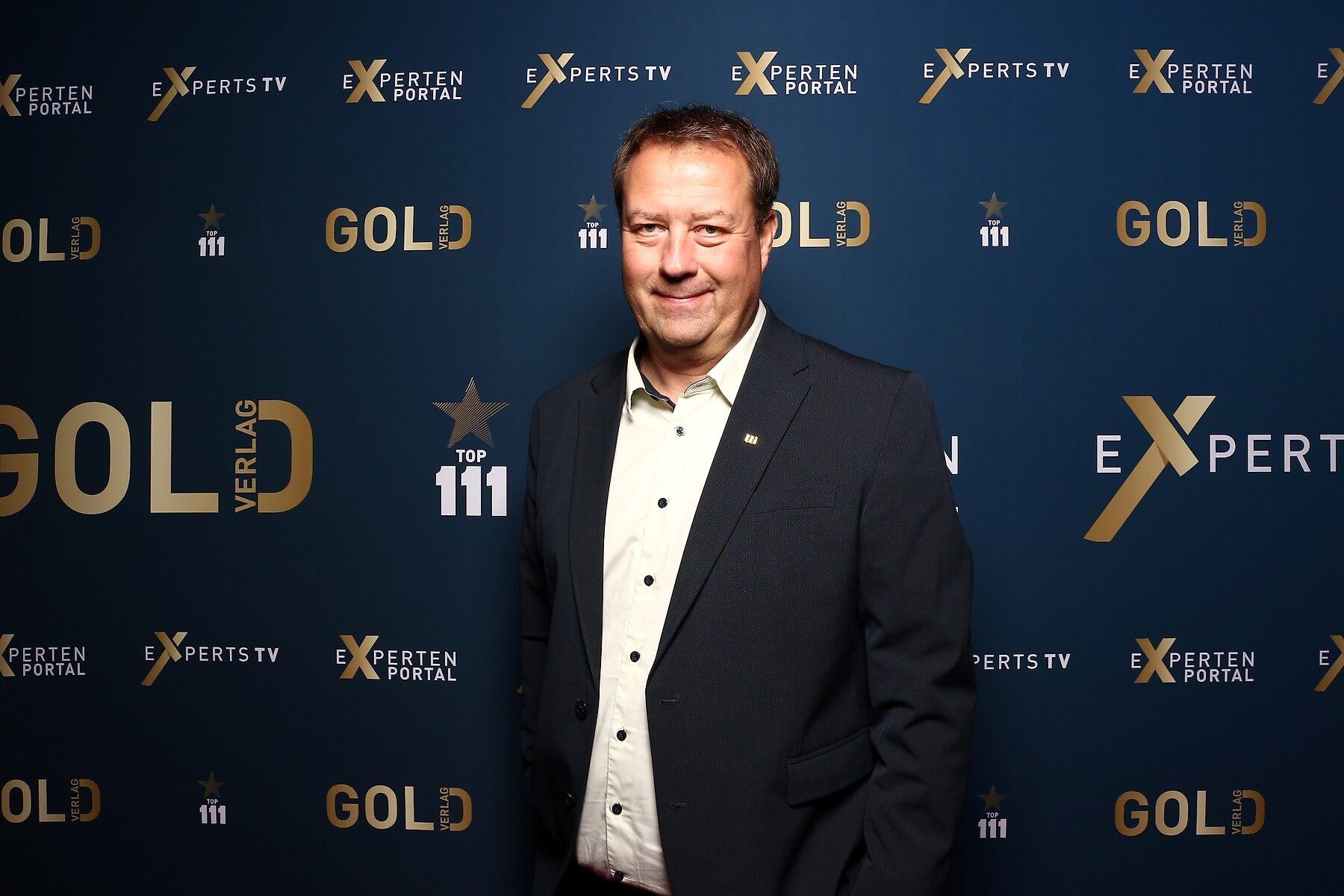 Birger Nispelim Anzug lächelt vor einem blauen Hintergrund mit goldener Schrift und Logos.