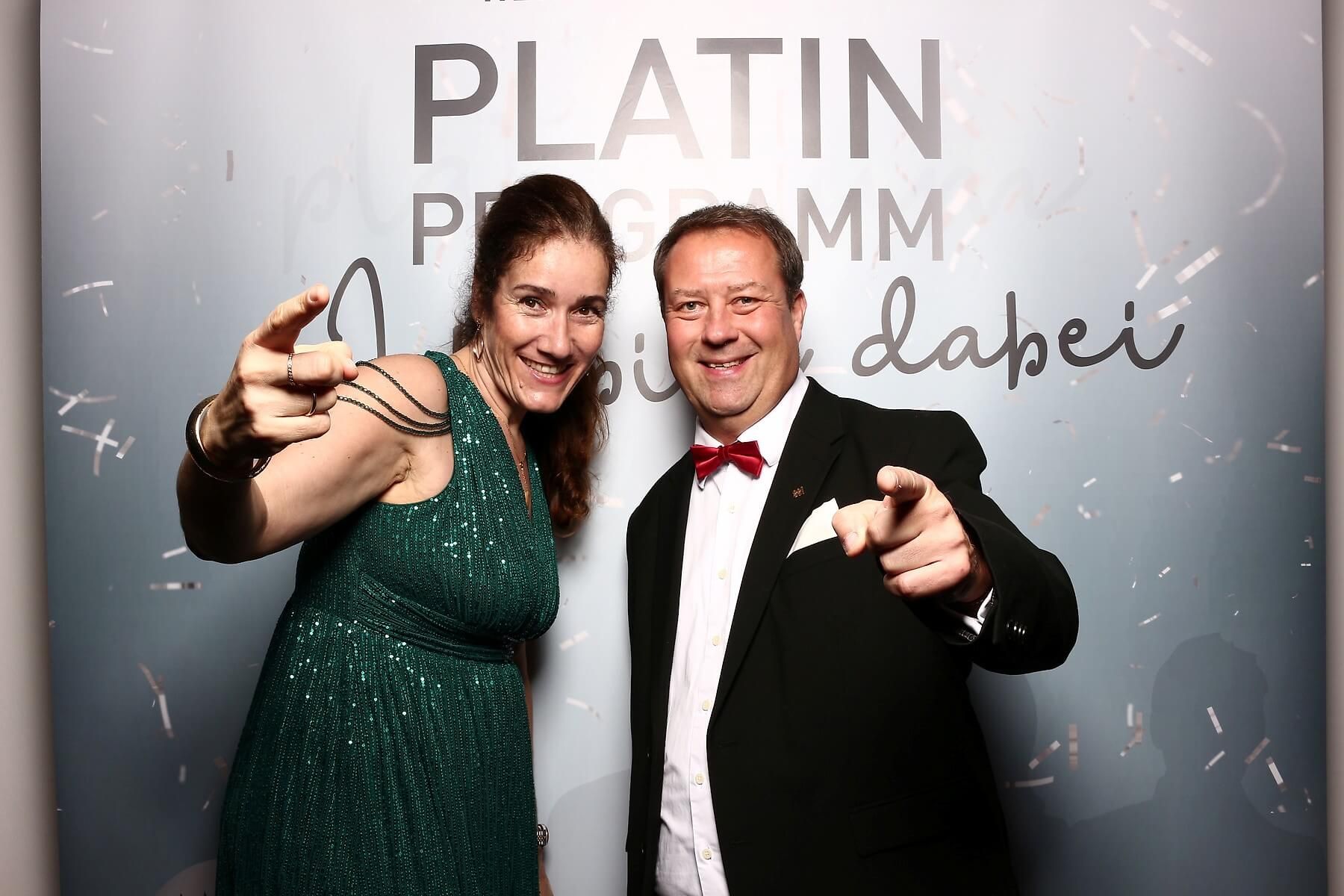 Frau im grünen Kleid und Birger Nispel im Anzug zeigen auf den Betrachter; Hintergrundtext „PLATIN PROGRAMM“.