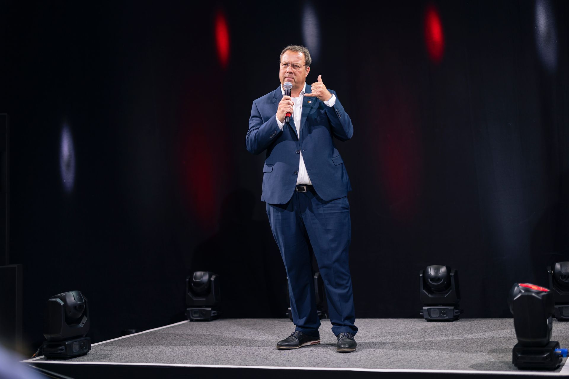 Ein Mann im Anzug steht auf einer Bühne und hält ein Mikrofon.