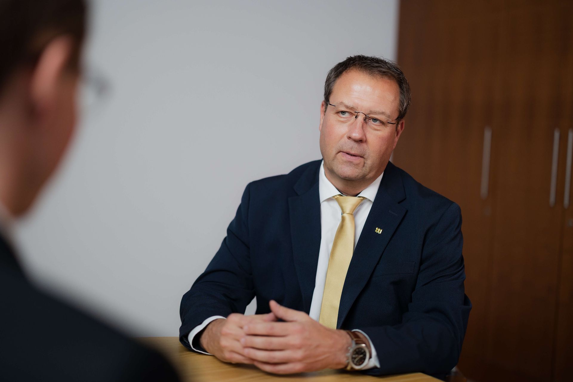 Birger Nispel im Anzug sitzt an einem Tisch und unterhält sich mit einer anderen Person.