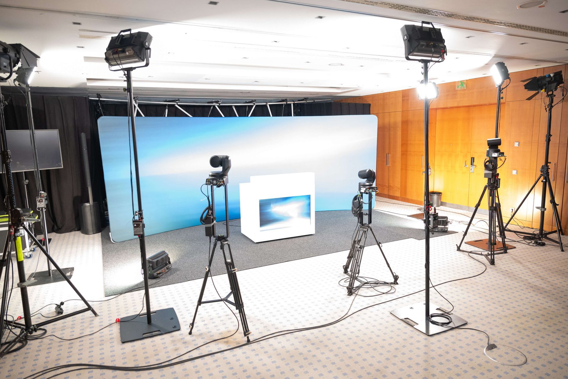 Ein Studioaufbau mit Kameras auf Stativen und hellen Scheinwerfern, die auf einen blauen Hintergrund gerichtet sind.