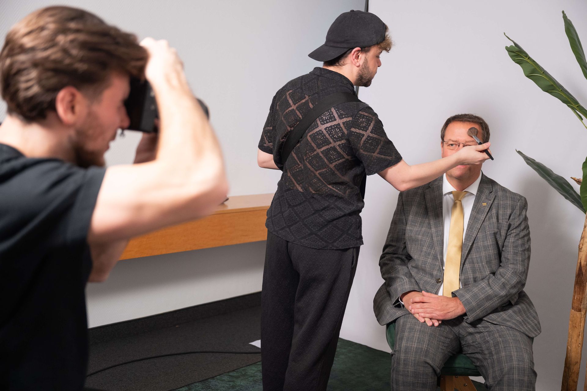 Ein Fotograf fotografiert Birger Nispel, der in einem Studio von einer anderen Person geschminkt wird.