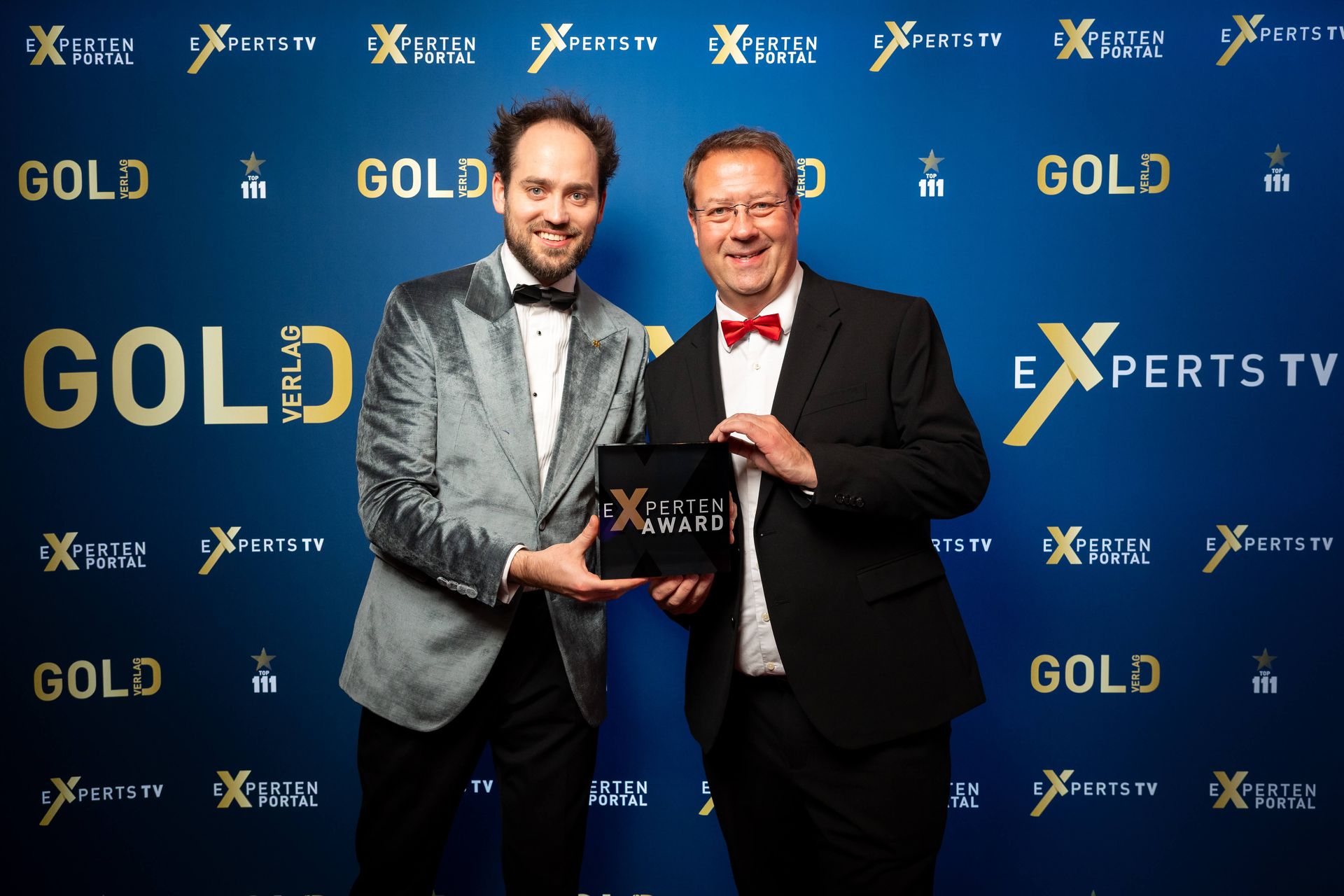 Birger Nispel udn Josua Laufer halten eine Auszeichnung vor einem blauen Hintergrund mit dem Logo „Experts TV Gold“.