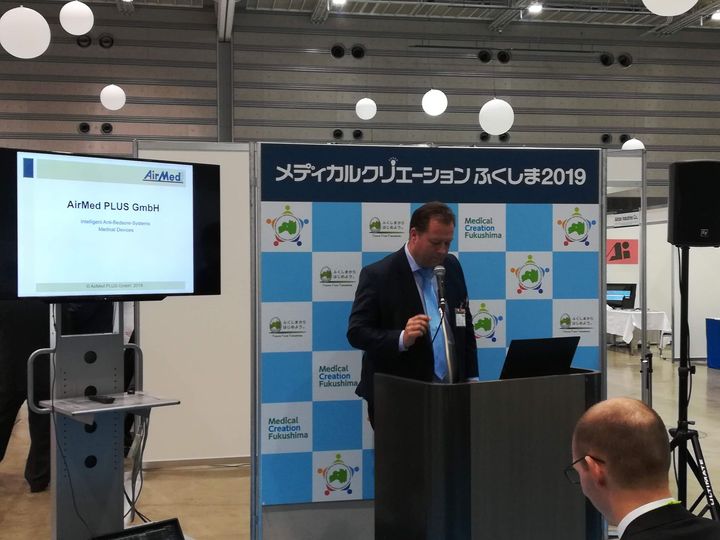 Ein Mann steht an einem Podium und hält vor einer großen Leinwand eine Präsentation.