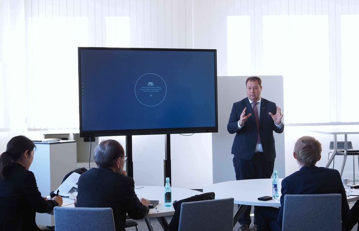 Ein Mann hält vor einer Gruppe von Menschen in einem Konferenzraum eine Präsentation.