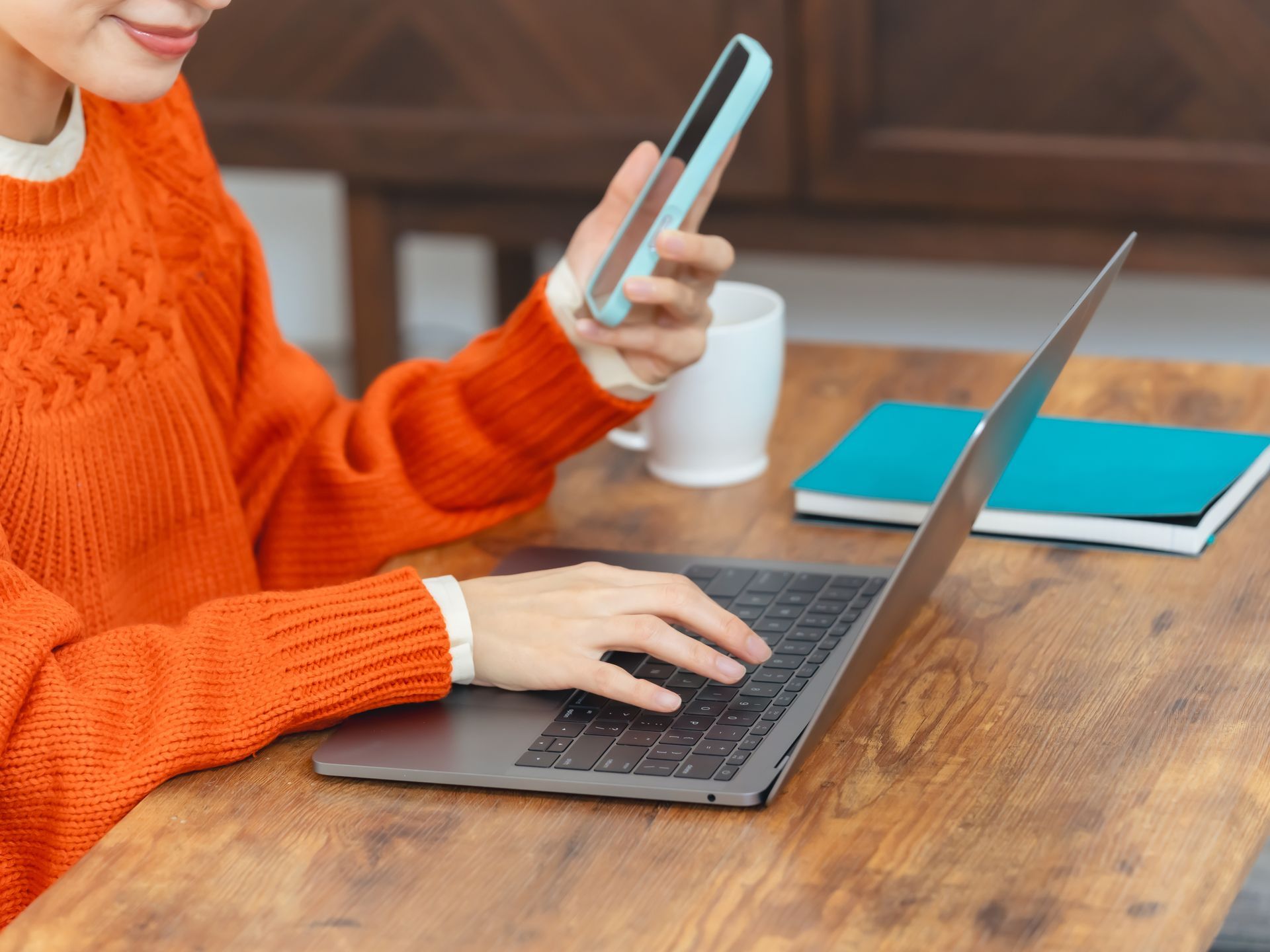 Femme tenant son téléphone devant son ordinateur portable.