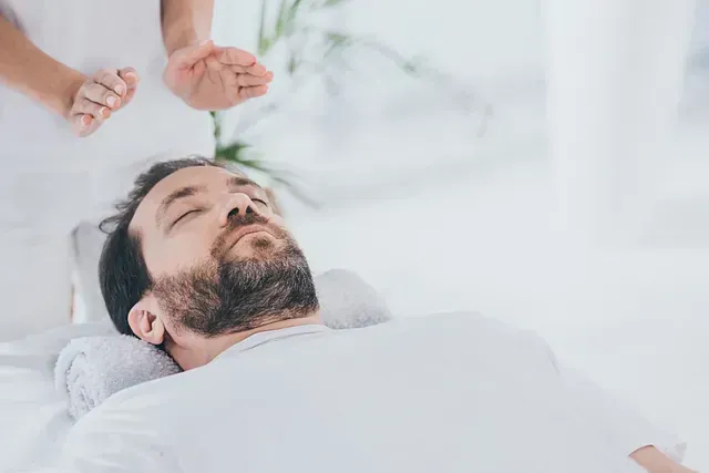 Un hombre con barba está acostado en una cama recibiendo un tratamiento de reiki.