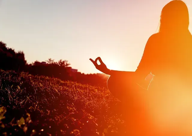 Una mujer está meditando en un campo al atardecer.