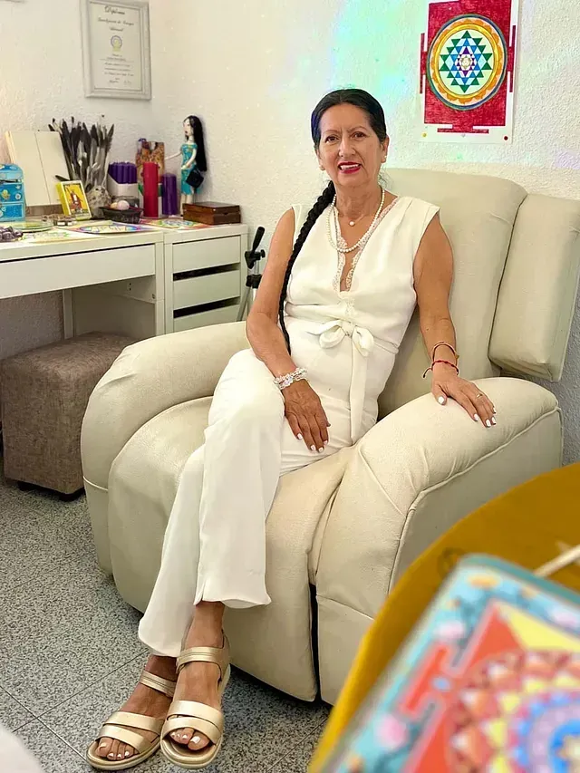 Una mujer con un mono blanco está sentada en una silla blanca.