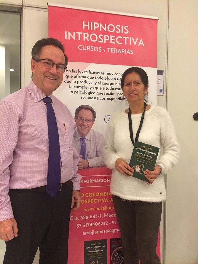 Dos personas de pie junto a un cartel rosa del curso y la terapia 