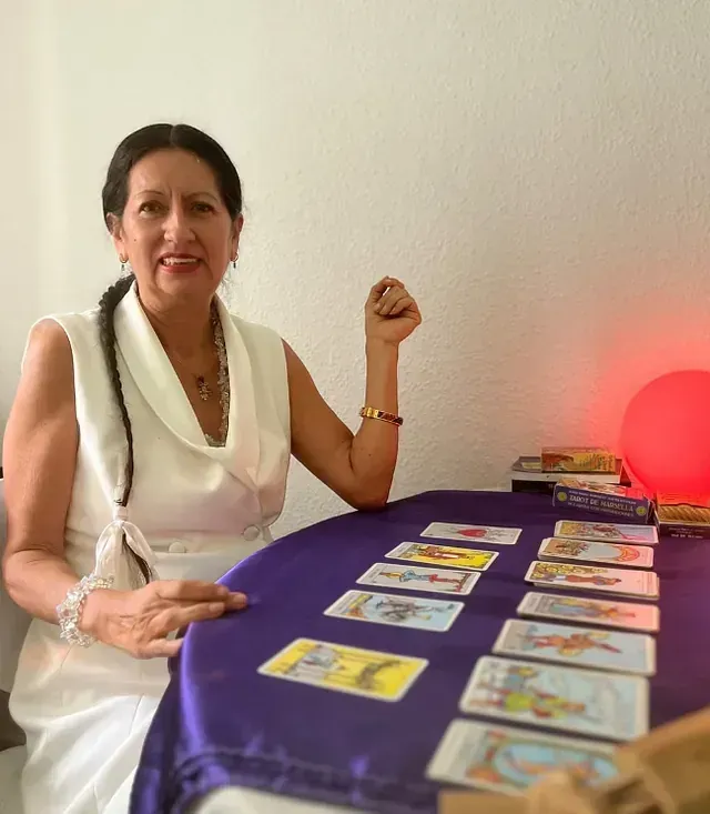 Una mujer está sentada en una mesa con cartas del tarot.