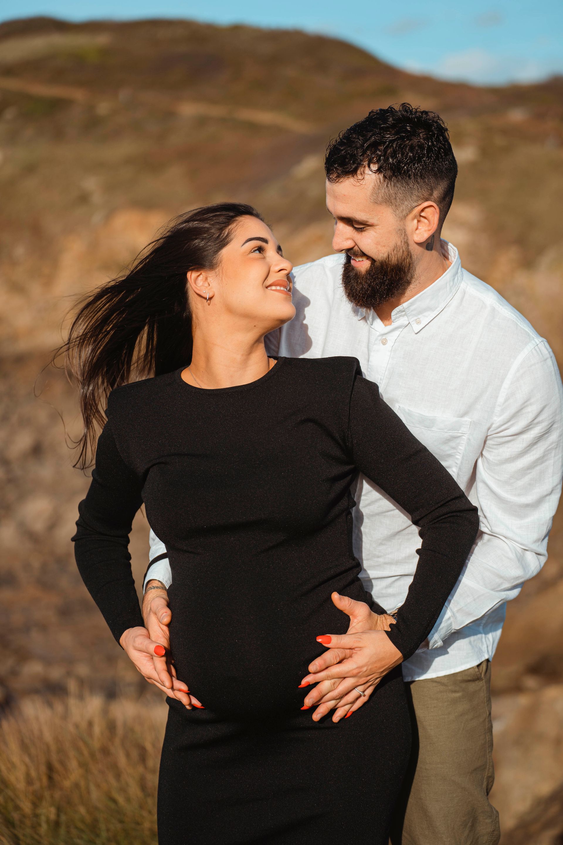 Une femme enceinte et un homme se regardent, les mains sur le ventre ; à l'extérieur.