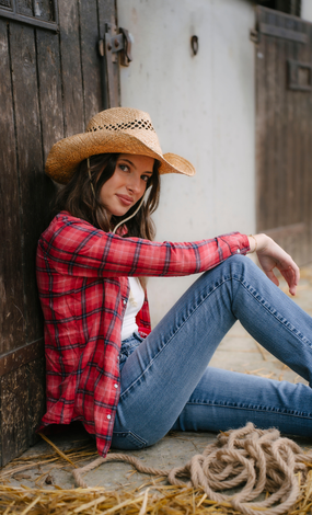 Une femme portant un chapeau de cow-boy et une chemise à carreaux est assise par terre.