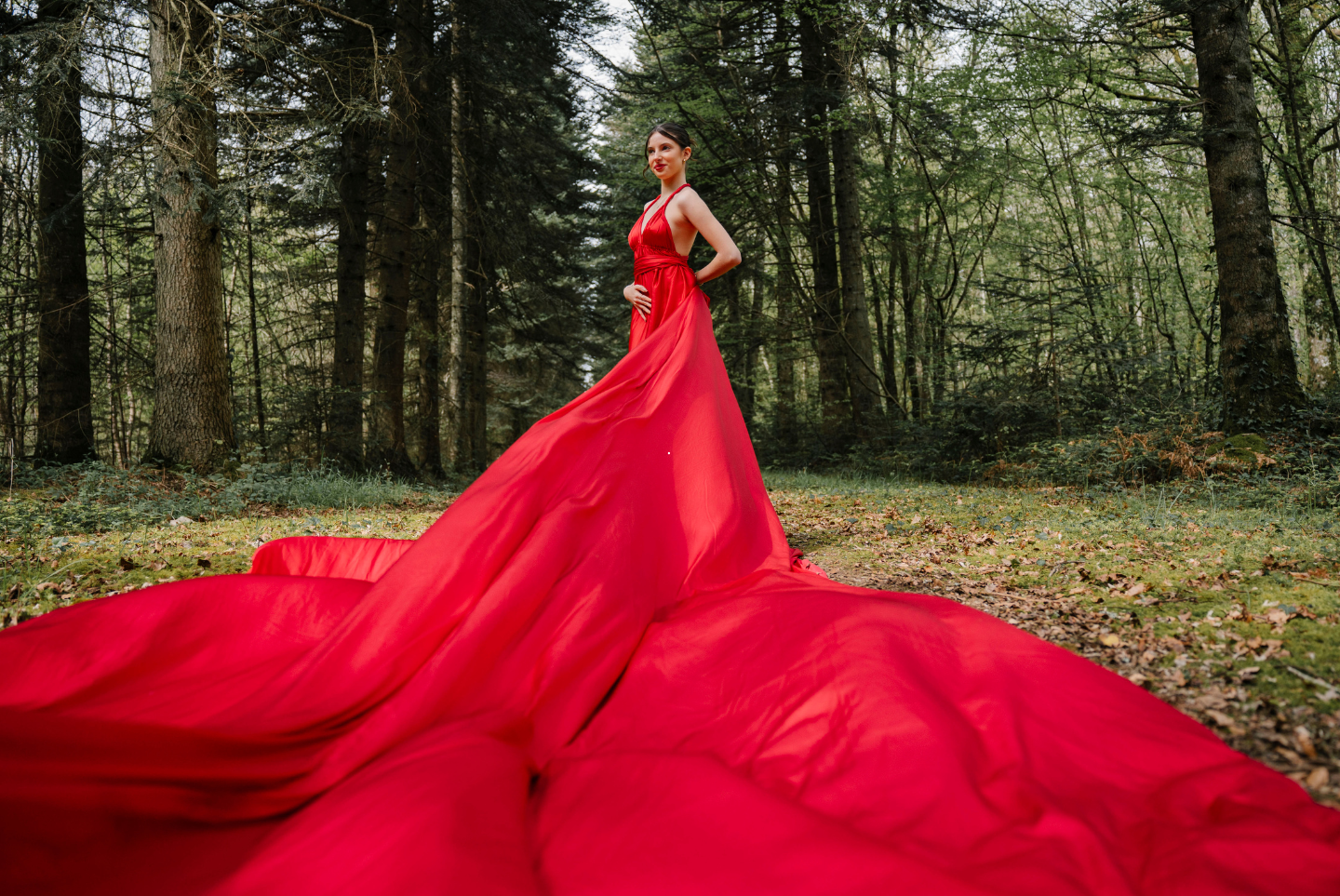 Une femme vêtue d'une longue robe rouge se tient au milieu d'une forêt.