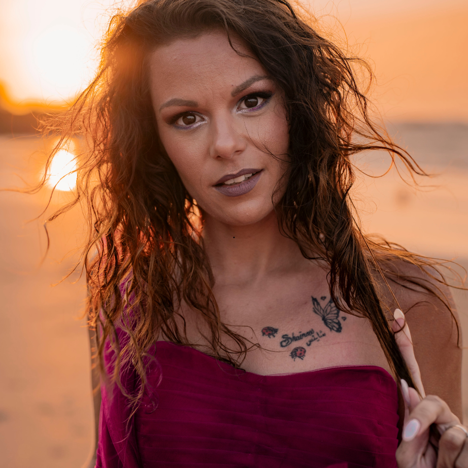 Une femme avec un tatouage de papillon sur la poitrine se tient sur une plage au coucher du soleil.