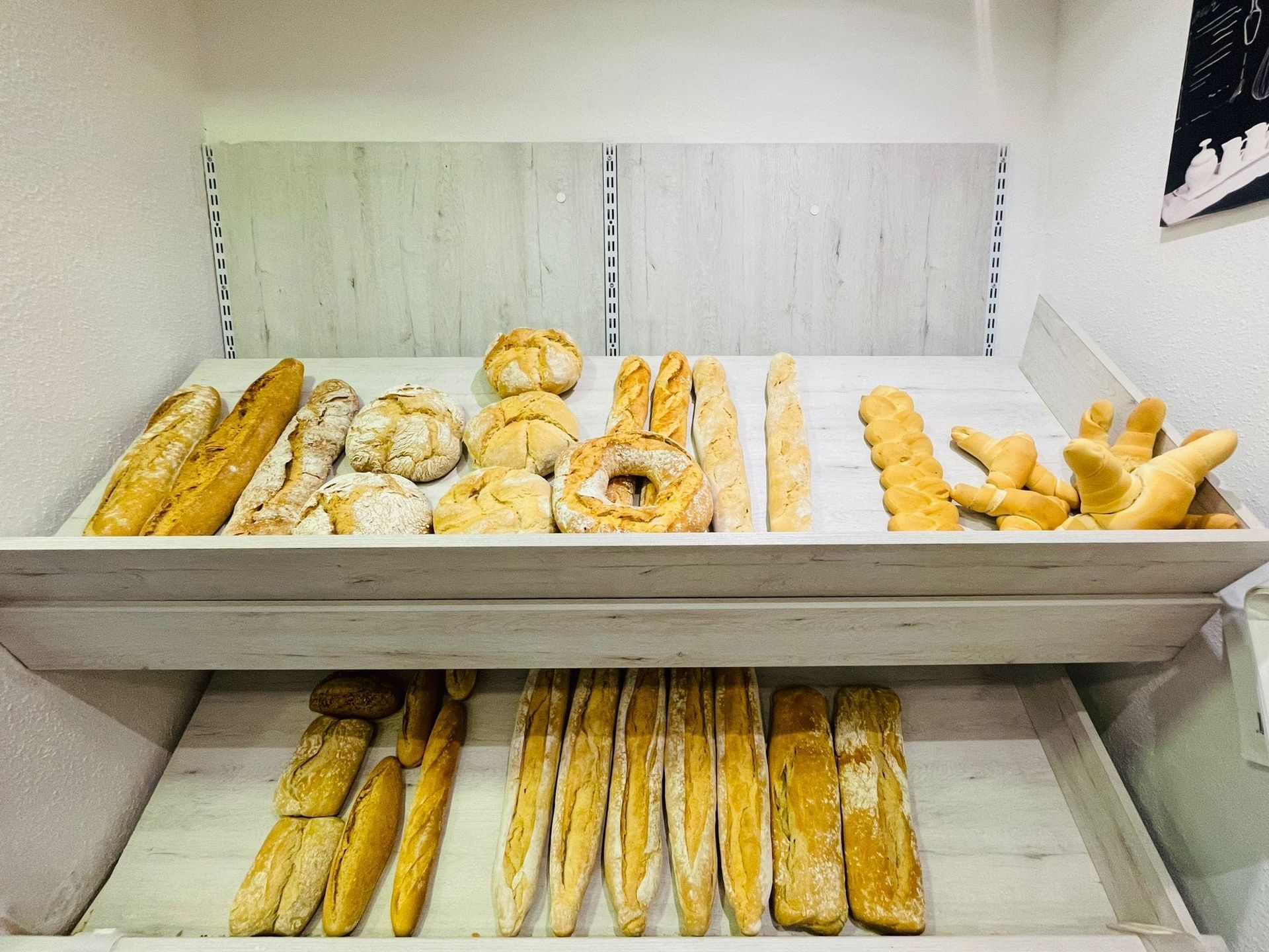 Vitrina de panadería llena de panes y bollos variados sobre estantes blancos.