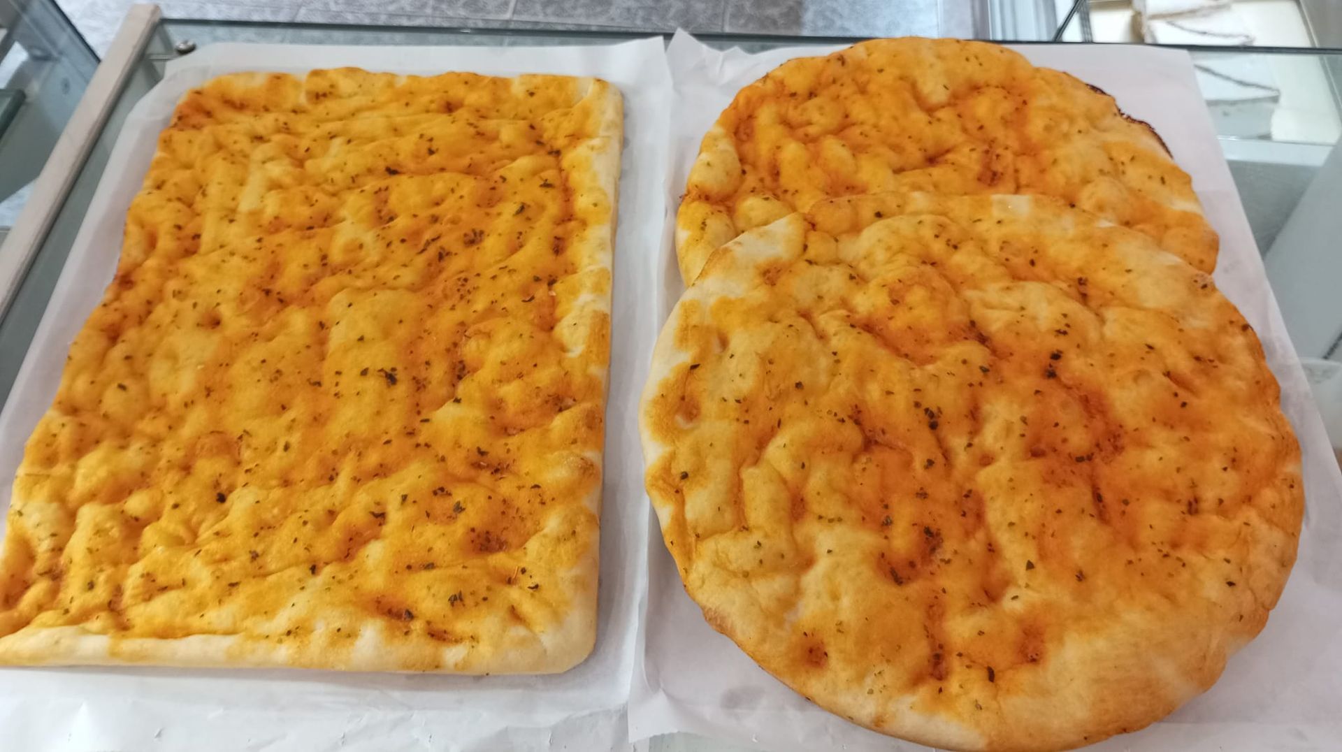 Dos panes dorados recién horneados sobre bandejas forradas con papel pergamino, uno rectangular y otro ovalado.