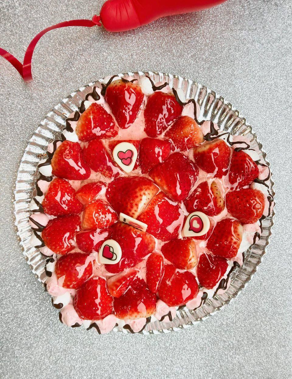 Tarta de fresas cubierta con fresas en rodajas y decoraciones en forma de corazón en una bandeja de aluminio.