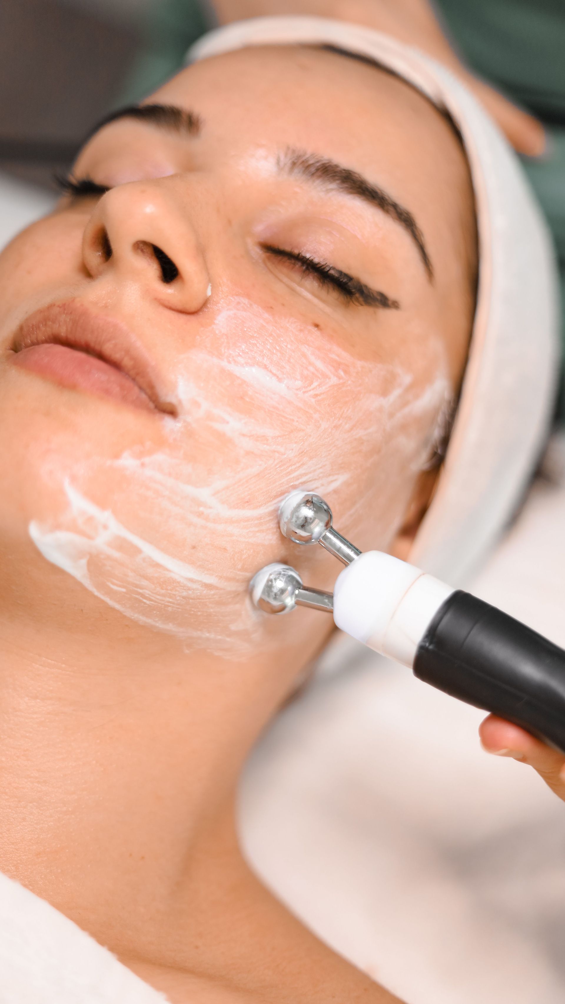 Tratamiento facial con aplicación de crema mediante un masajeador manual en la mejilla del cliente.