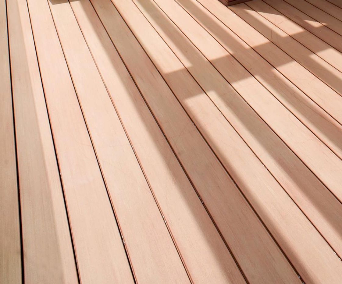 Una terraza de madera con el sol proyectando sombras sobre ella.