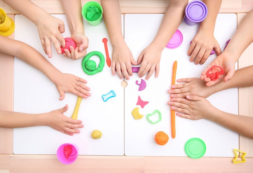 Kitareinigung | Kinderhände spielen mit bunter Modelliermasse auf einem Tisch.