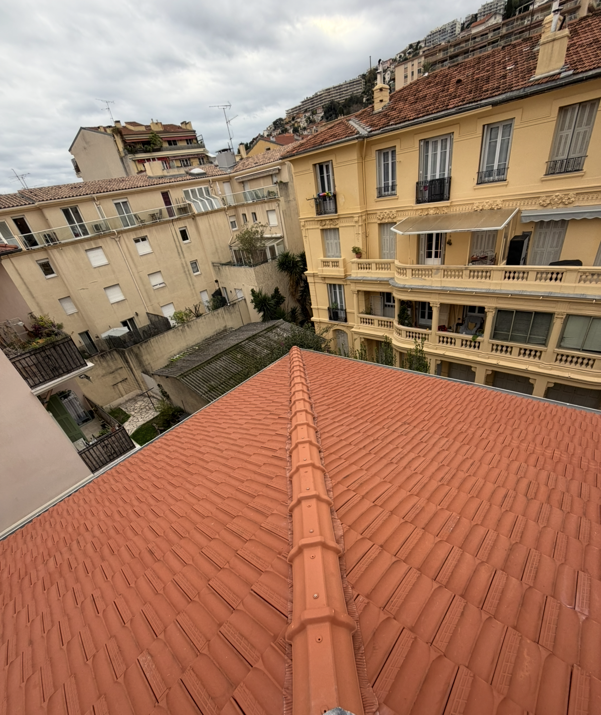 Toit de tuiles rouges, avec des immeubles d'appartements jaunes de style méditerranéen en arrière-plan.