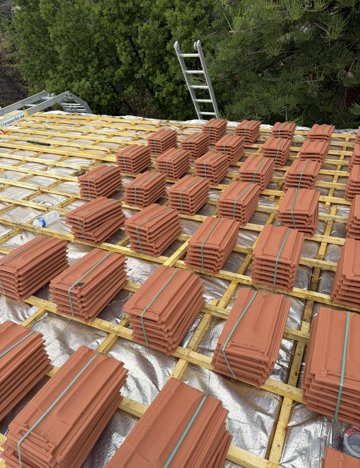 Des piles de tuiles rouges disposées en rangées sur une grille en bois recouvrant une surface réfléchissante sur le toit d'un bâtiment.