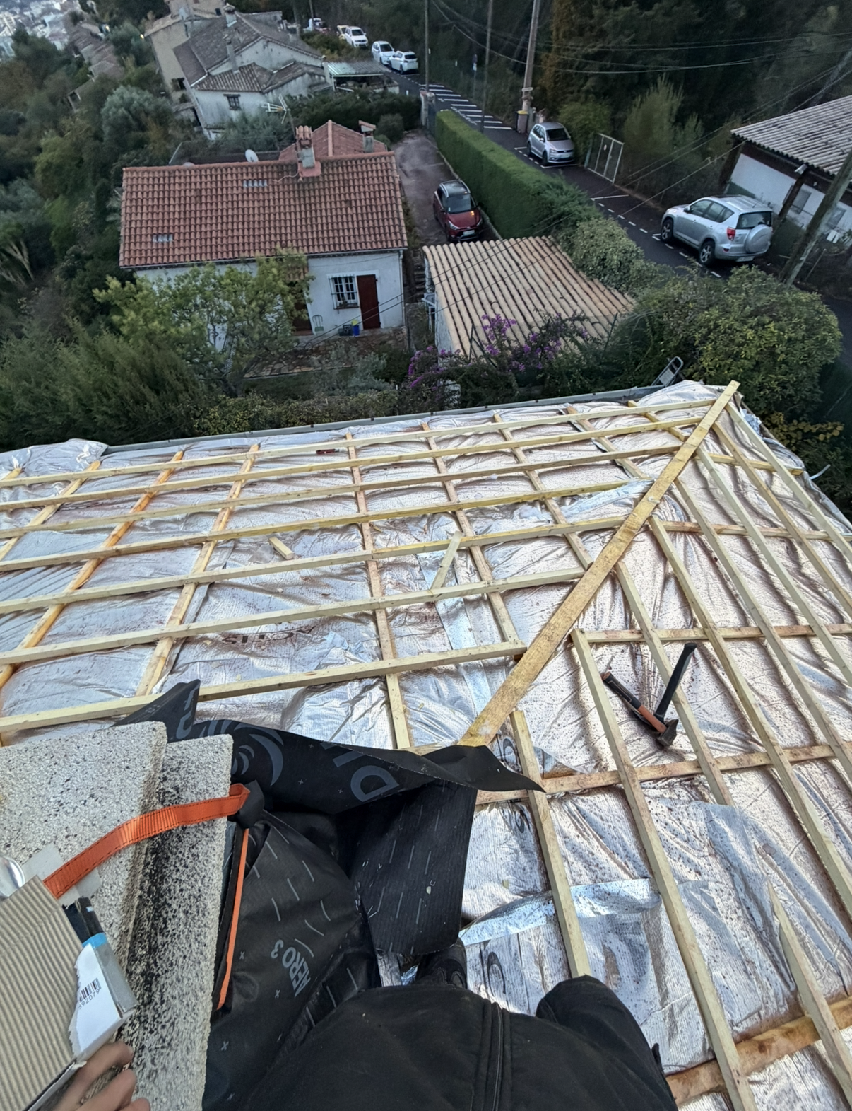 Toit en construction, montrant une structure en treillis de bois recouvrant un isolant réfléchissant au-dessus d'un quartier.