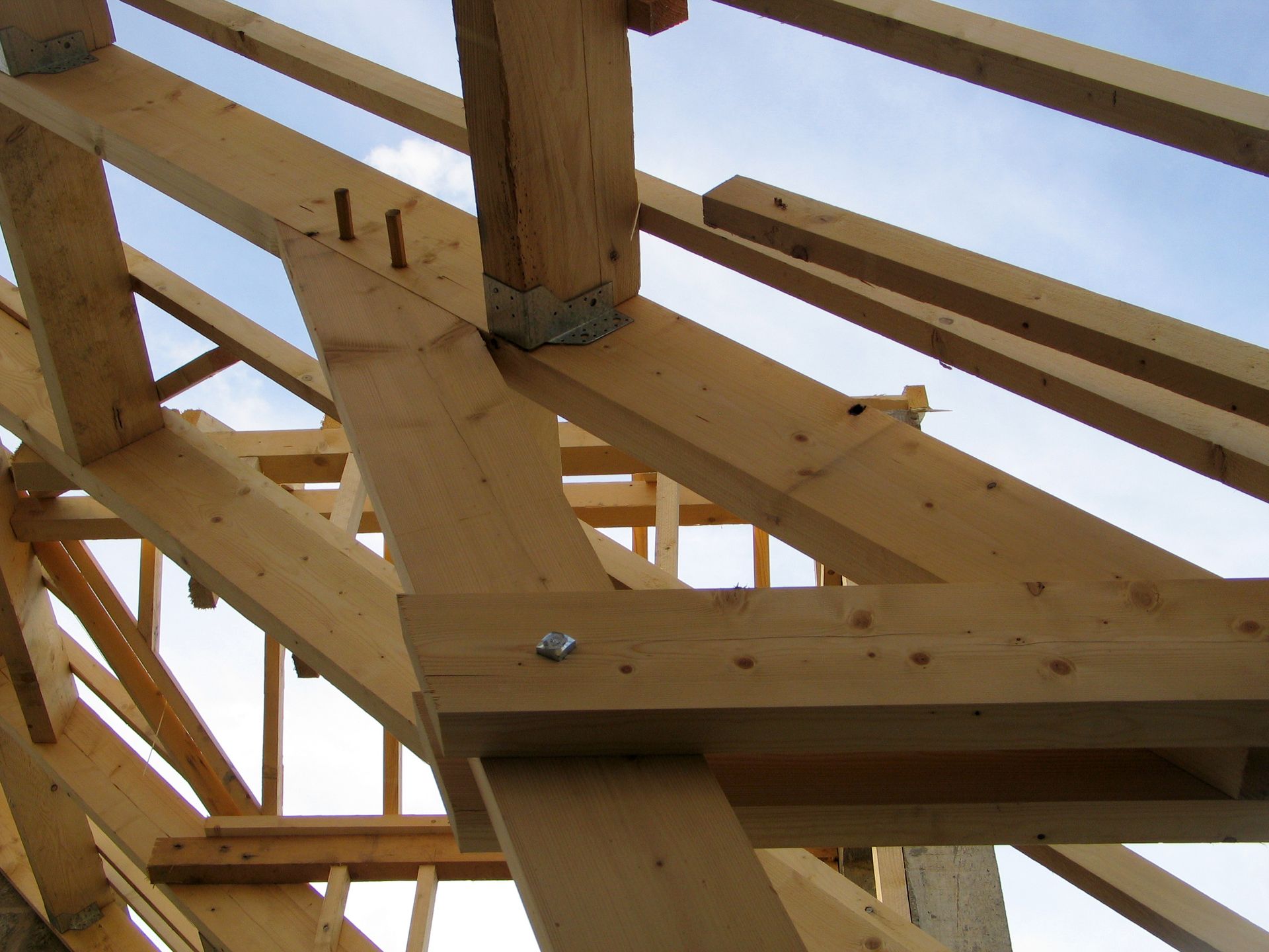 Vue en contreplongée d'une charpente de toit en bois en construction, sur fond de ciel bleu.