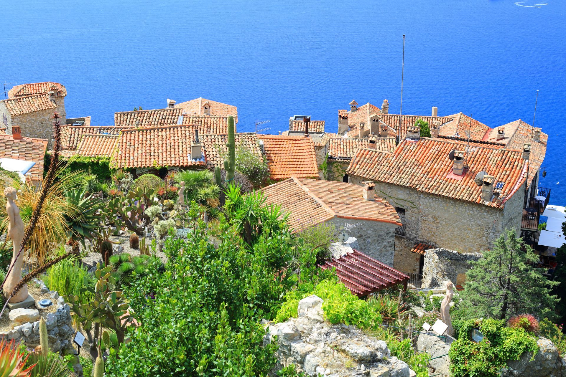 Un village méditerranéen perché sur une colline, avec ses bâtiments en pierre aux toits de tuiles rouges, surplombant la mer.