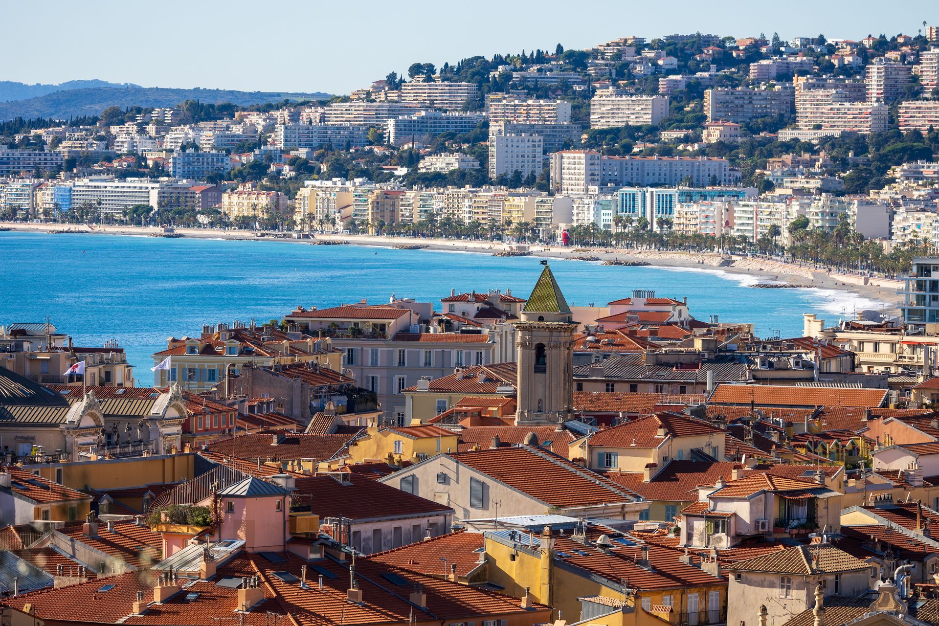 Vue aérienne de Nice, montrant des toits de tuiles orangées s'étendant jusqu'à un littoral bleu turquoise.