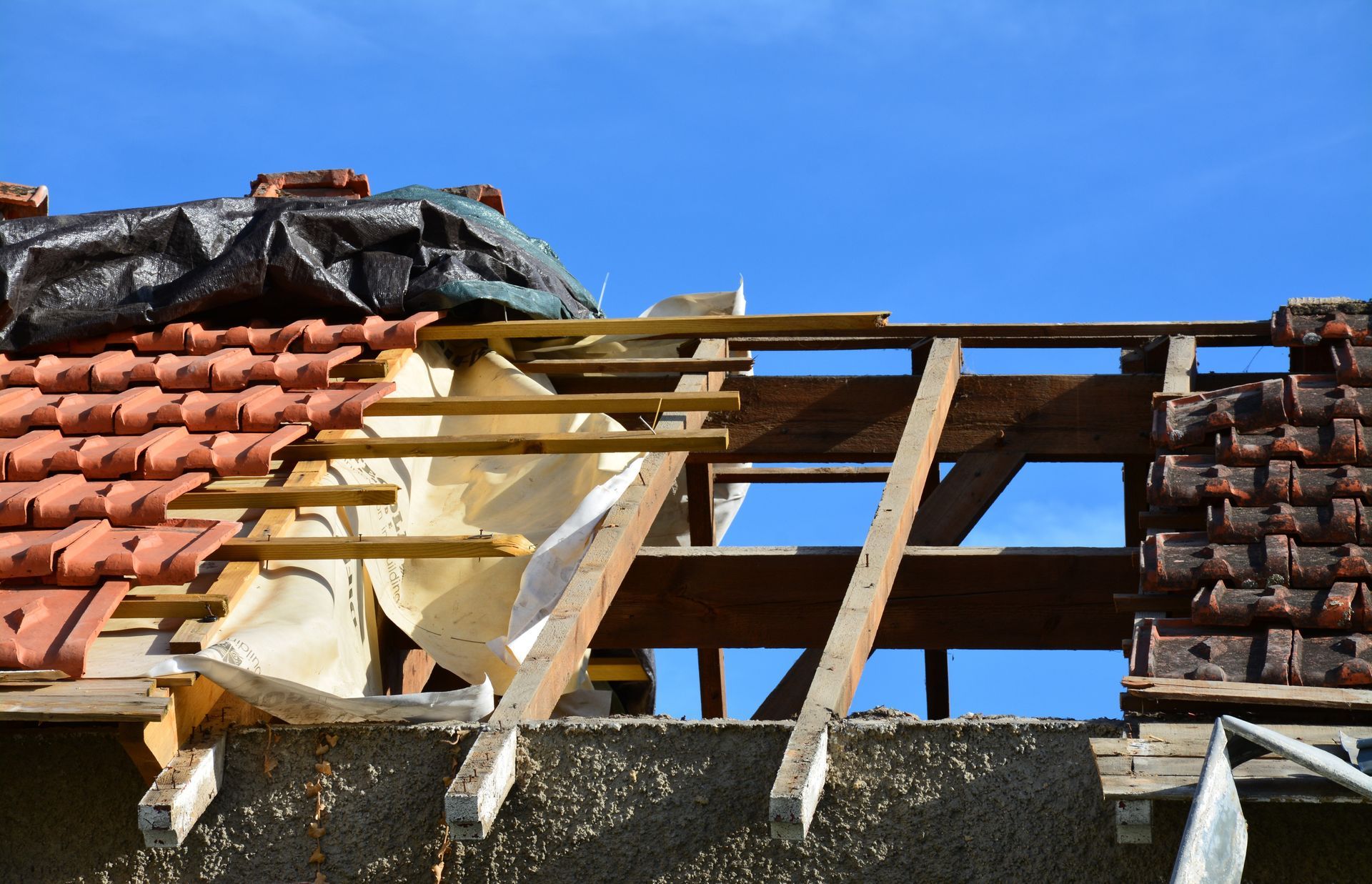 Toiture d'une maison en construction avec des tuiles partiellement posées, des chevrons en bois et une bâche de protection.