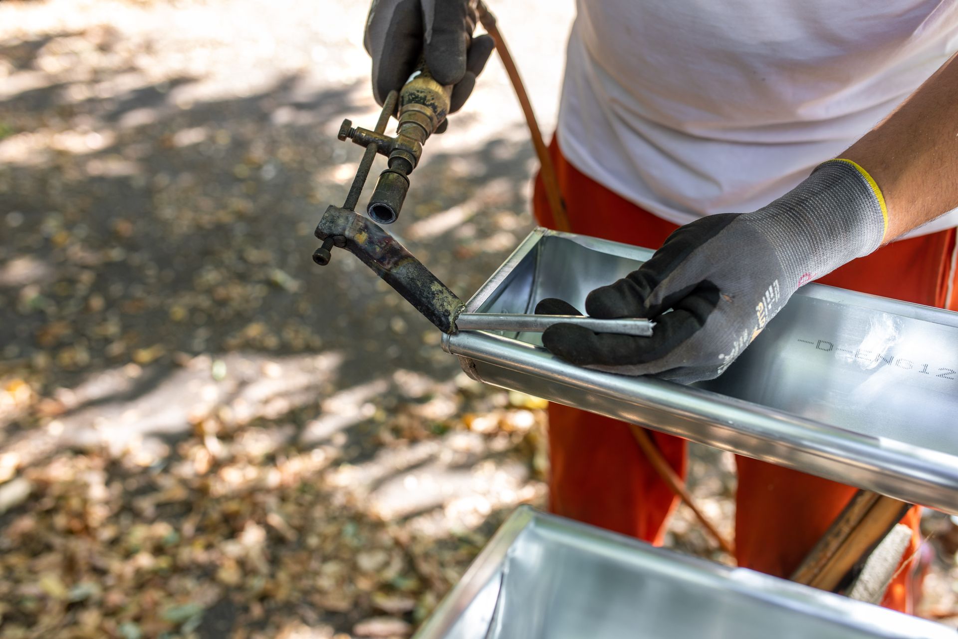 Une personne portant des gants utilise un fer à souder pour réparer une gouttière métallique.