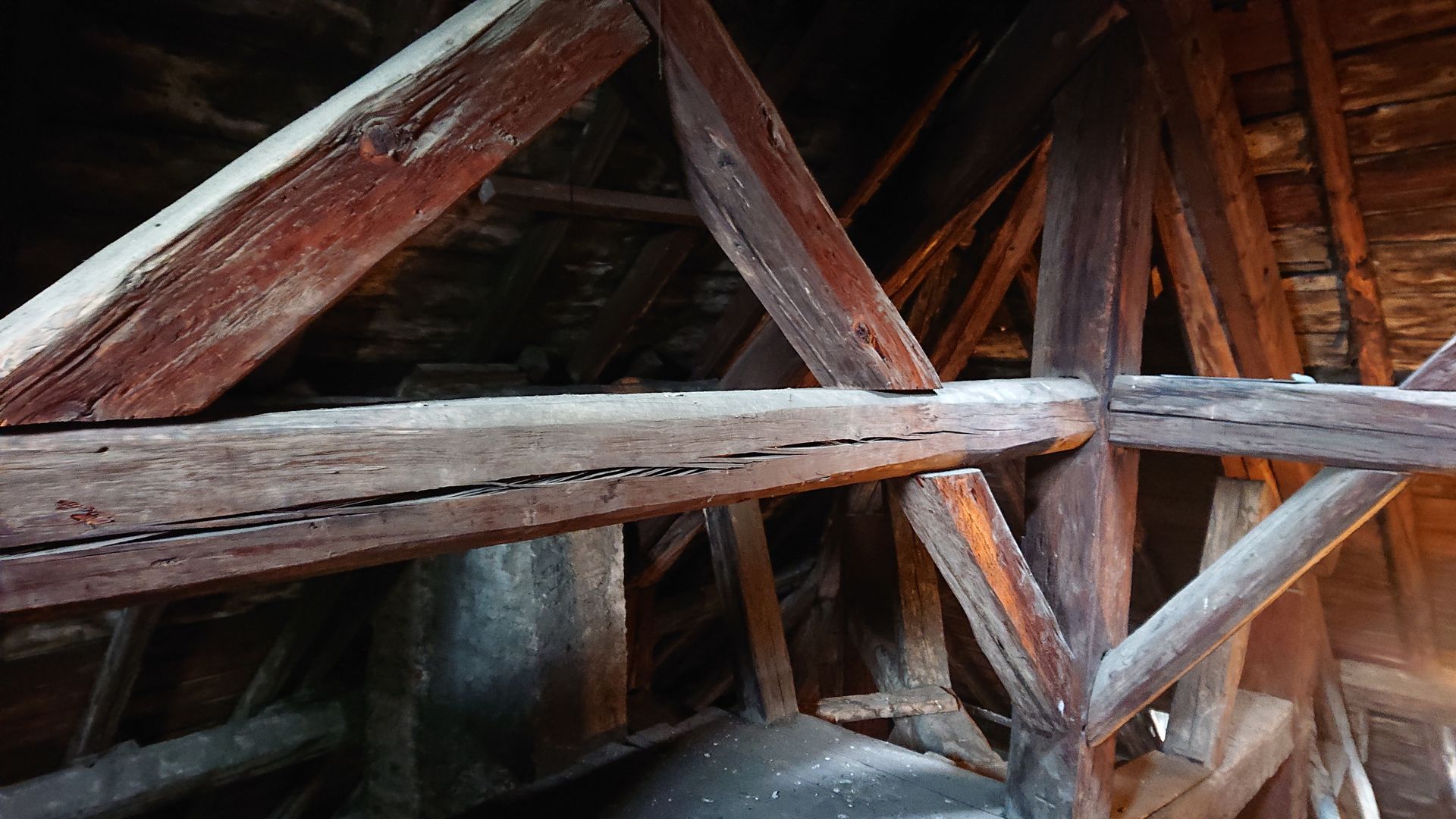 Intérieur de grenier avec charpente et poutres de soutien en bois patiné, sous une structure de toit en pente.