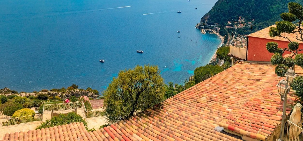Vue en plongée de toits de tuiles rouges surplombant une ville côtière et la mer d'un bleu profond.