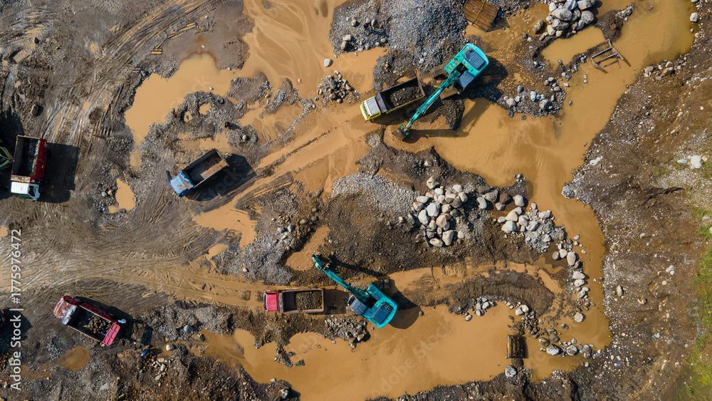 Veduta aerea di escavatori e autocarri ribaltabili al lavoro in un cantiere edile immerso nel fango.