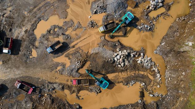 Veduta aerea di escavatori e autocarri ribaltabili al lavoro in un cantiere edile immerso nel fango.