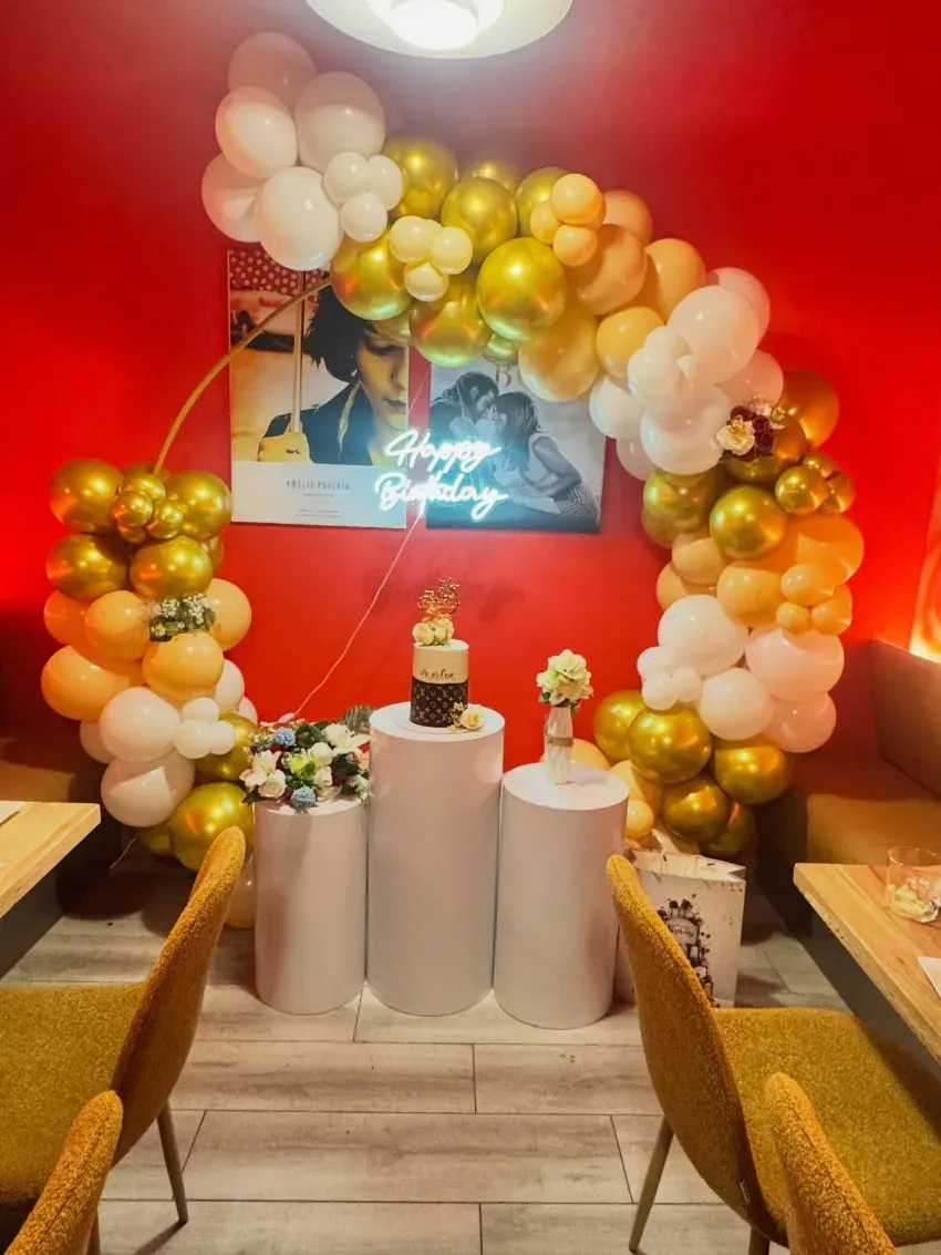 Arco de globos y decoración de pastel en un local de fiesta rojo con globos dorados, blancos y color crema.