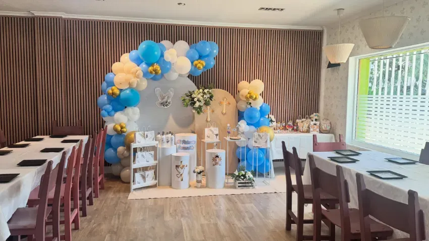 Mesa de postres decorada con globos en un local de fiestas con detalles en azul, blanco y dorado.