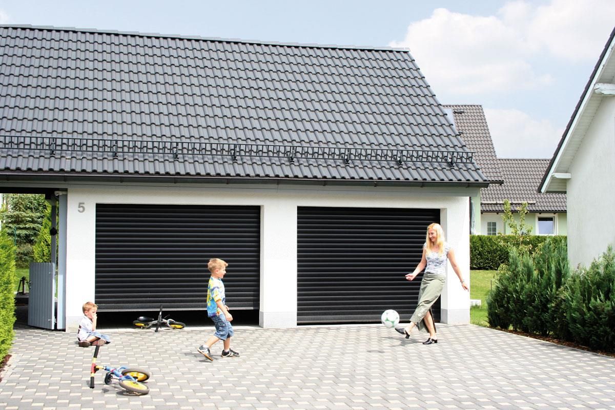 Eine Frau und zwei Kinder spielen mit einem Fußball vor einem Garagentor