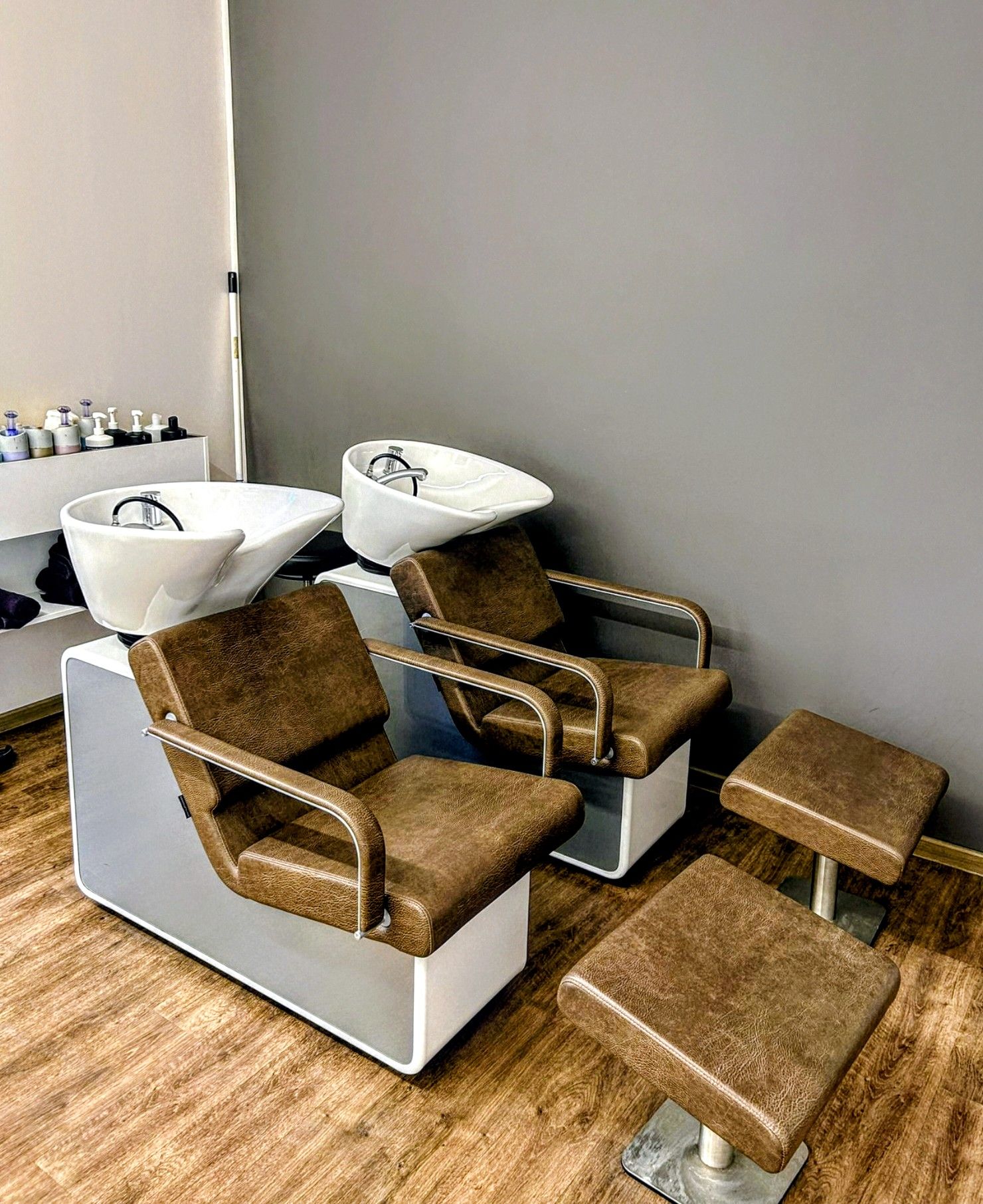 Zwei Haarwaschplätze mit braunen Stühlen, weißen Waschbecken und passenden Fußstützen im Friseursalon Kagel in Werder.